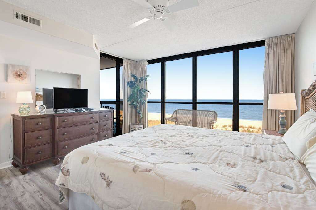 Quarto com uma cama grande, televisão em uma cômoda e vista para a praia.