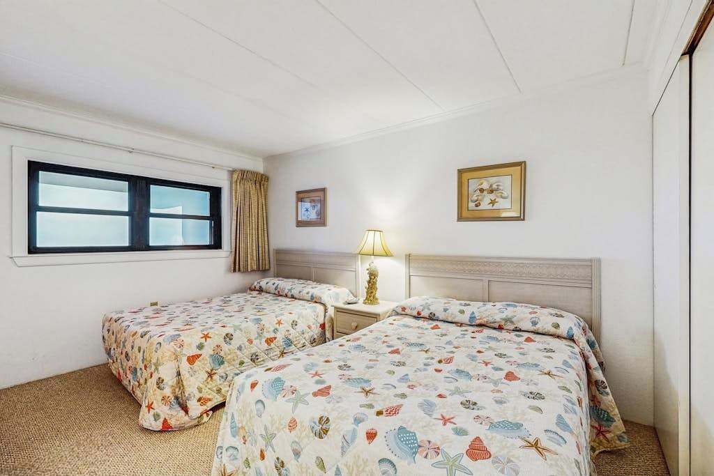 A hotel room with two beds, a window, a lamp, and a framed picture on the wall.