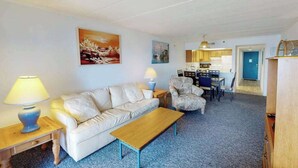 A living room with a sofa, coffee table, and lamps. There is a dining area with chairs and a table. - Beachfront Suite w/Ocean Views From Balcony, Free WiFi, Central AC, Private W/D (Ocean City)