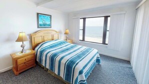 A bedroom with a bed, two bedside tables, a window with a view of the sea, and a painting on the wall. - Beachfront Suite w/Ocean Views From Balcony, Free WiFi, Central AC, Private W/D (Ocean City)