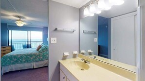 A bedroom with a bed, a bathroom with a sink and mirror, and a balcony with a view. - Fountainhead Towers 906 (Ocean City)