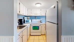 A narrow kitchen with white cabinets, a microwave, a stove, and a refrigerator. - Fountainhead Towers 906 (Ocean City)