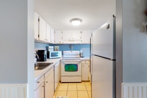 A narrow kitchen with white cabinets, a microwave, a stove, and a refrigerator. - Fountainhead Towers 906 (Ocean City)
