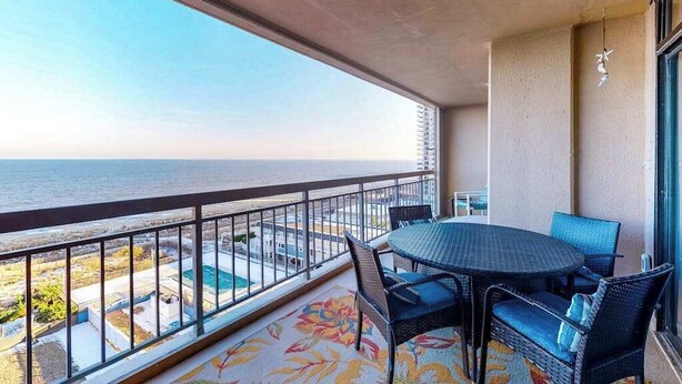 A balcony with a view of the ocean, a round table, and wicker chairs. - Fountainhead Towers 906 (Ocean City)