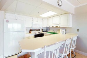 A kitchen with white cabinets, a refrigerator, a microwave, a sink, and a dining area with chairs. - Sunny Beachfront Condo w/Private Balcony, Washer/Dryer, A/C, Free WiFi, Views (Ocean City)