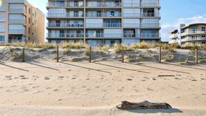 Ein mehrstöckiges Hotel mit Balkonen, direkt an einem Sandstrand mit Dünen im Hintergrund gelegen.