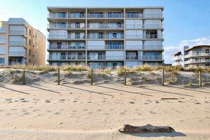 A multi-story hotel with balconies, situated on a sandy beach with dunes in the background. - Sunny Beachfront Condo w/Private Balcony, Washer/Dryer, A/C, Free WiFi, Views (Ocean City)