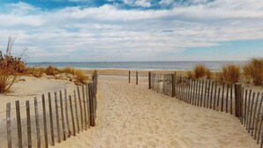 Een zandpad langs het strand dat naar de oceaan leidt, met een houten hek aan beide kanten.