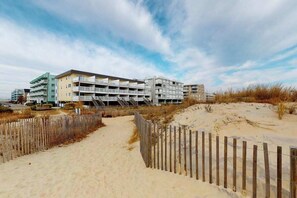 Ein Strandhotel mit mehreren Etagen, einem sandigen Pfad und einem Holzzaun.