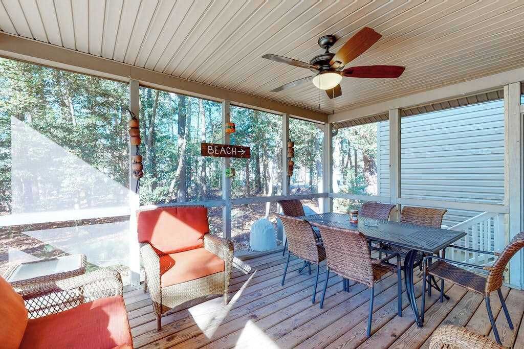 A covered outdoor area with a table and chairs, a sign indicating a beach direction, and a ceiling fan.