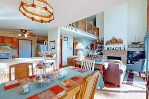 A spacious living area with a fireplace, a dining table with a colorful tablecloth, and a cozy seating arrangement. - Dove Lane 8 (Ocean Pines)