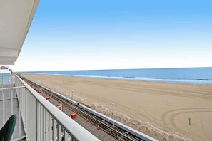 Blick auf einen Sandstrand und das Meer vom Balkon mit Geländer.