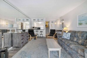 Ein Wohnzimmer mit Sofa, Couchtisch, Fernseher und einer Küchenzeile inklusive Kühlschrank und Herd.