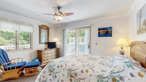 Ein Schlafzimmer mit Bett, Deckenventilator, Schminktisch, Stuhl, Fernseher und einem Gemälde.