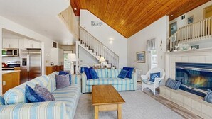 Ein geräumiges Wohnzimmer mit gestreiften Sofas, einem Holztisch, einem Kamin und einer Treppe zu einer oberen Ebene.