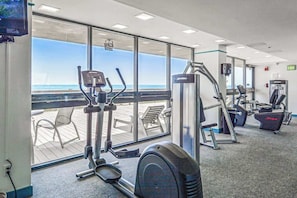A gym with cardio machines, weight machines, and a view of the ocean through large windows. - Convenient Condo in Gorgeous Oceanfront Location w/Shared Pool, Free WiFi (Ocean City)