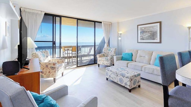 Une chambre d’hôtel moderne dotée d’un balcon, d’un canapé, d’un fauteuil, d’une petite table et d’un téléviseur.