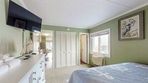 Un dormitorio con cama, televisor, cómoda, ventana y puerta.