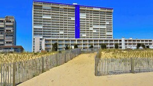 Ett stort hotell med flera våningar och balkonger, en sandstig som leder till entrén och en klarblå himmel.