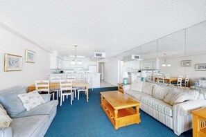 A living room with a sofa, a coffee table, a dining table with chairs, and a kitchen area. - Waterfront condo with balcony, views, pools, gym, & sauna (Ocean City)