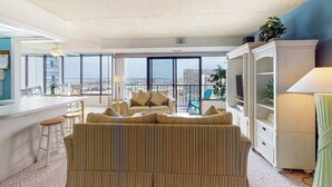 Una sala moderna con sofá, un comedor con sillas, un balcón con vistas y un mueble blanco para entretenimiento.