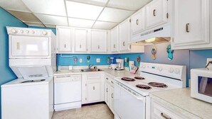 Una cocina con electrodomésticos blancos, paredes azules y suelo de baldosas.