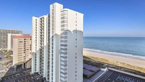 Un hotel moderno de gran altura con varios pisos, estacionamiento y vista a la playa.
