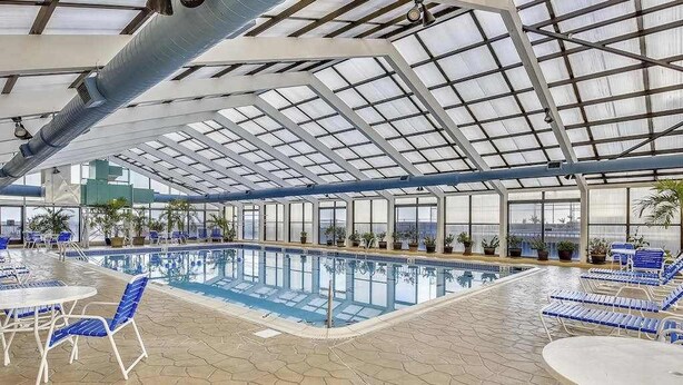 Una piscina interior con techos de vidrio transparente, sillones azules de descanso y plantas en macetas.