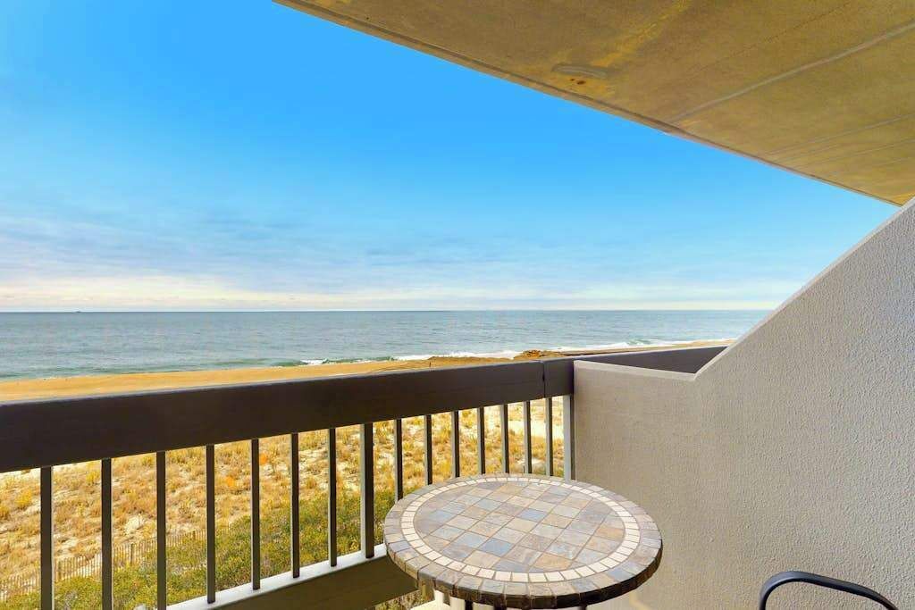 A balcony with a view of the ocean, a tiled table, and a chair.