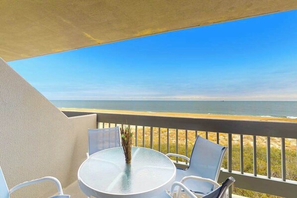 A balcony with a round table and chairs, overlooking a beach. - Wonderful Suite in Beachfront Complex w/Shared Pool, Free WiFi, Private W/D (Ocean City)
