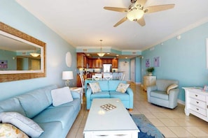 A living room with a ceiling fan, a sofa, a coffee table, and a dining area with a table and chairs. - Belmont Towers 708 (Ocean City)