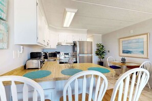 A modern kitchen with white cabinets, stainless steel appliances, and a wooden dining table with white chairs. - Breakaway East 206 (Ocean City)