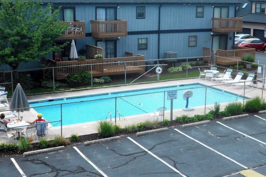 Une piscine dotée de chaises longues et d’une terrasse délimitée par une clôture, le tout entouré d’un immeuble à plusieurs étages avec des balcons.