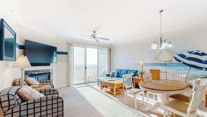 A room with a sofa, a dining table with chairs, a ceiling fan, and a view of the ocean through large windows. - Belmont Towers 505 (Ocean City)