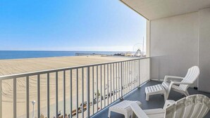 A balcony with a view of the beach, white chairs, and a railing. - Belmont Towers 505 (Ocean City)