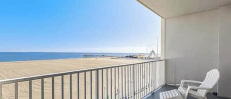Uma varanda com vista para a praia, cadeiras brancas e um corrimão.