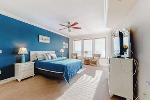 Ein Schlafzimmer mit einem Bett, Nachttischen, einem Schreibtisch, einem Sessel, einem Deckenventilator und einem Fernseher.