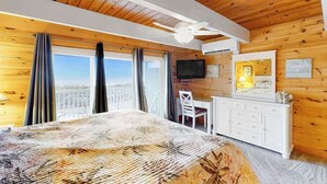 A wooden-paneled room with a bed, a desk, a chair, a television, and a balcony with curtains. - Beachwalk 6 (Ocean City)