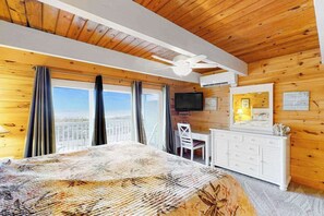 A wooden-paneled room with a bed, a desk, a chair, a television, and a balcony with curtains. - Beachwalk 6 (Ocean City)