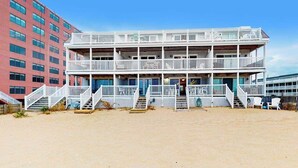 A multi-story building with balconies, a staircase, and a sandy ground. - Beachwalk 6 (Ocean City)