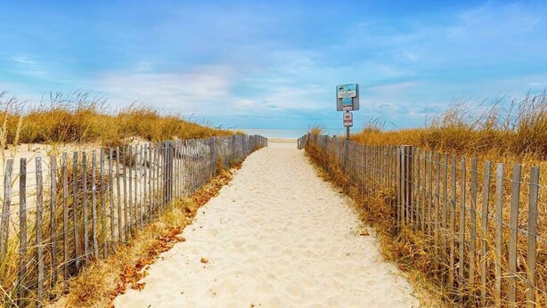A sandy pathway flanked by wooden fences leading to a beach. - Beachwalk 6 (Ocean City)