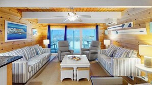 A room with wooden walls, a ceiling fan, two sofas, a coffee table, and a view through large windows. - Beachwalk 6 (Ocean City)