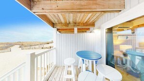 A wooden deck with a glass door leading to a room, white railings, and a view of the beach. - Beachwalk 6 (Ocean City)