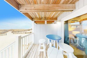 A wooden deck with a glass door leading to a room, white railings, and a view of the beach. - Beachwalk 6 (Ocean City)