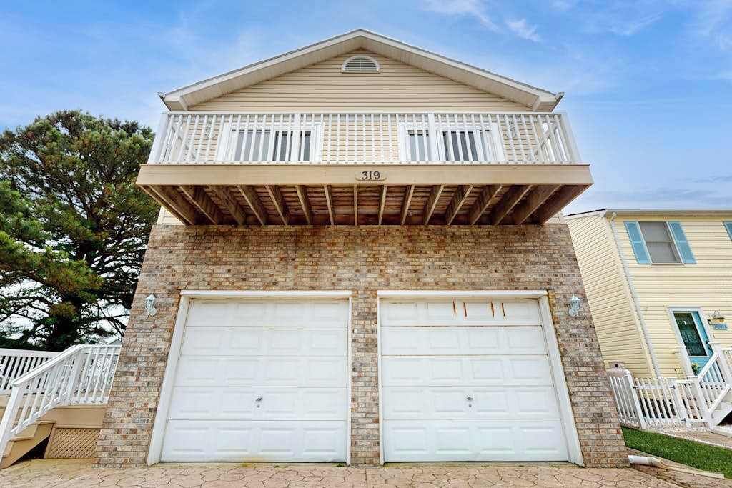 Edifici de dues plantes amb un balcó, dues portes de garatge i façana de maó.