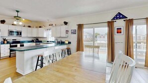 Une cuisine moderne dotée d’un îlot central, de meubles blancs et d’un coin repas avec une grande table et des chaises.