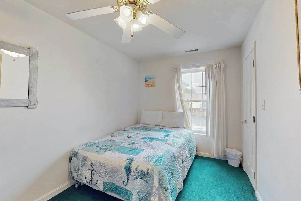 Une chambre à coucher avec un lit, un ventilateur de plafond, une fenêtre avec des rideaux et une porte.