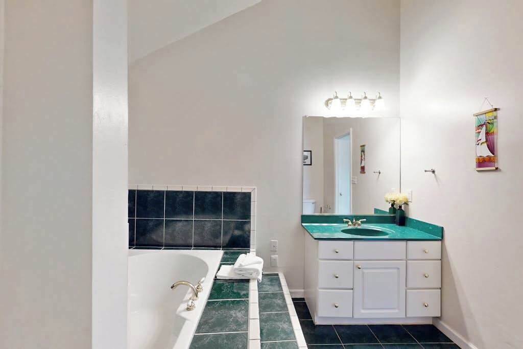 A bathroom with a bathtub, a sink with a green countertop, and a mirror with lights.