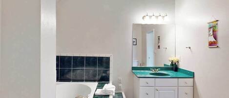 A bathroom with a bathtub, a sink with a green countertop, and a mirror with lights.