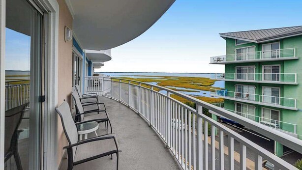Ein Balkon mit Stühlen, Blick auf den Strand und ein mehrstöckiges Gebäude mit vielen Fenstern.